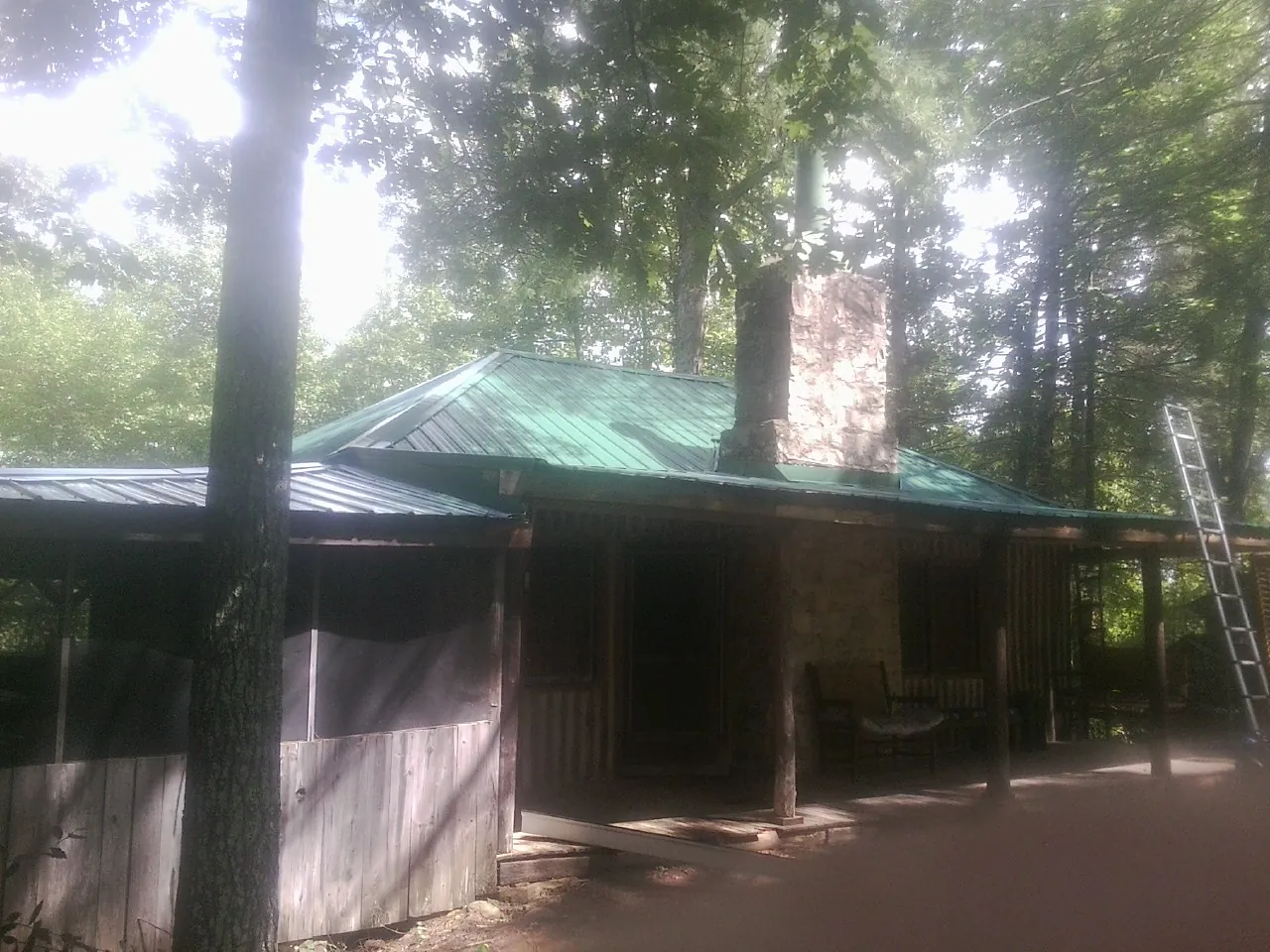 Green metal roof and stone chimney above a log cabin porch in Clifton
